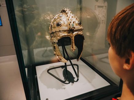 Trier, Römischer Soldatenhelm im Landesmuseum © Travelisto Junge vor Glasvitrine mit prunktvollem Römerhelm