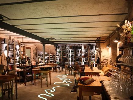 Traben-Trarbach, Innenbereich der Vinothek Blick in eine Vinothek mit Holztischen und Stühlen und großem Weinregal