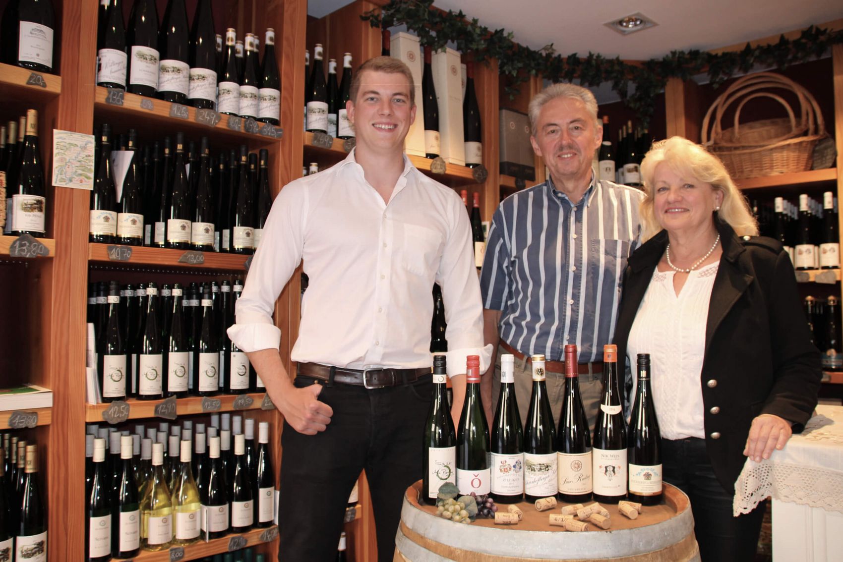 Saarburg, Inhaber der Vinothek Bonsai & Wein © Bonsai & Wein - Die Vinothek der Saar Drei Personen vor Weinfass mit Weinflaschen in ihrer Vinothek