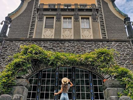 Traben-Trarbach, Villa Hüsgen bei Mythos Mosel © Elina Leitz Ansicht auf eine Frau mit Hut, in der Hand ein Glas Moselwein, mit Blick auf die Villa Hüsgen in Traben-Trarbach.