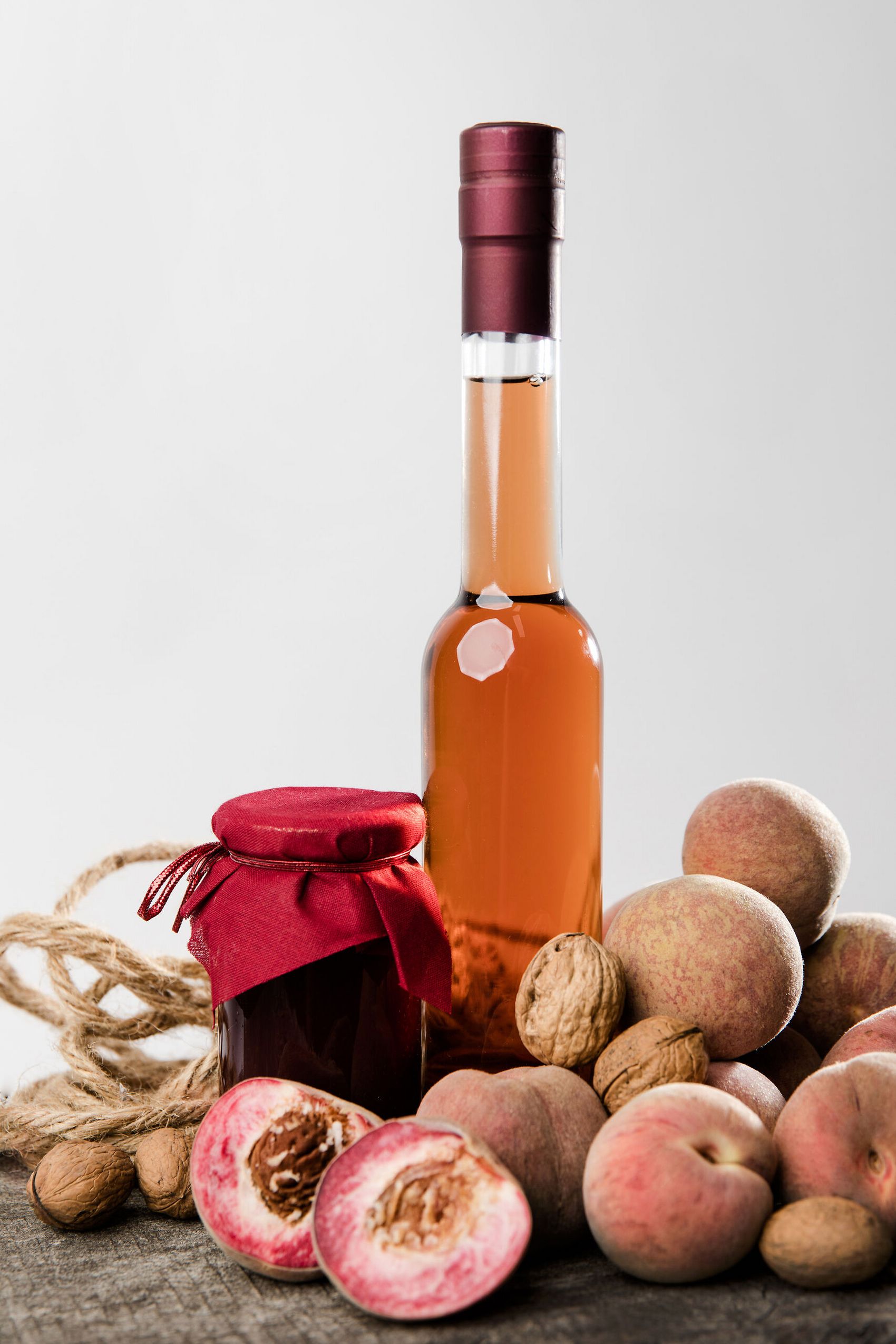 Moselweinbergpfirsich Produkte © Tourist-Information Ferienland Cochem Eine schmale Flasche Pfirsichlikör umgeben von reifen Pfirsichen und einem Glas Pfirsichmarmelade.